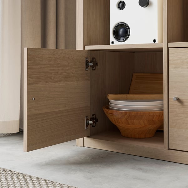 Wooden cabinet with open door revealing neatly stacked bowls and dishes. Dark hinges visible on door.
