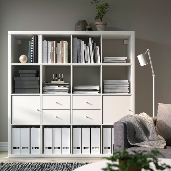 Ikea KALLAX shelf unit with books, drawers, and files. Beside a chair and lamp.