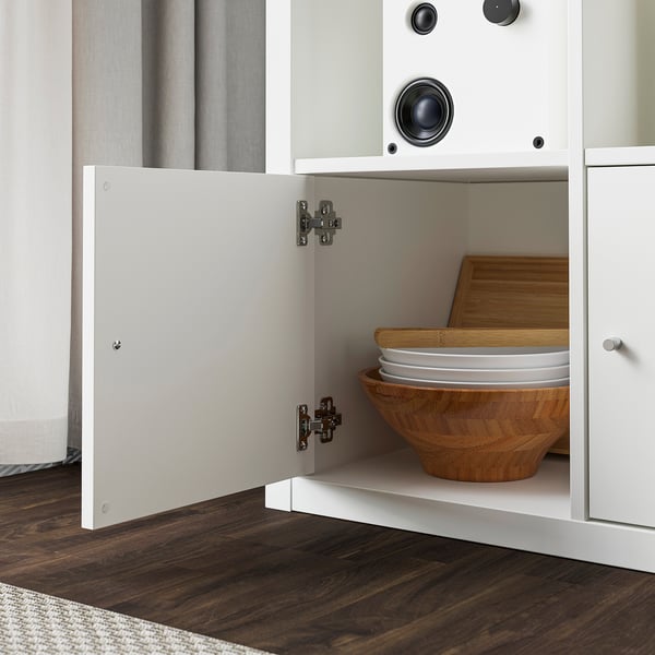 Open white cabinet showing wooden bowl, plates, and cutting board stored inside, with dark wood floor visible.