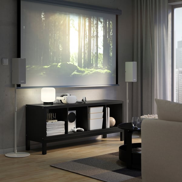 Modern living room with KALLAX shelf, speakers, and tv showing a forest, brown sofa, snacks, and wine.