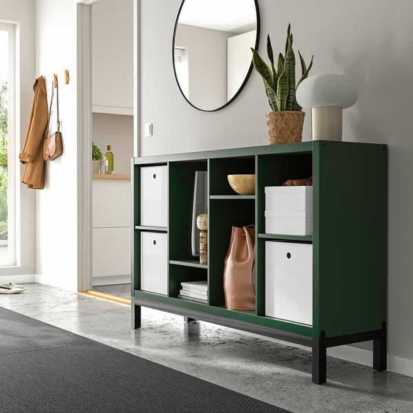 Modern KALLAX green shelf, holding decor & books. Mirror above, coat hangers to left, and decor items on top. Elegant, compact.
