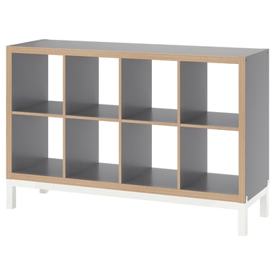 A KALLAX shelving unit in grey with a wooden frame, featuring multiple open compartments and white legs.