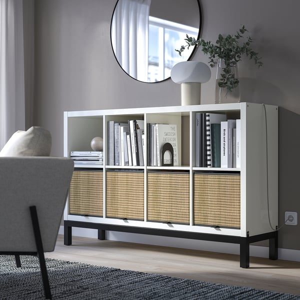 White KALLAX shelving with woven inserts, books, and mirror.