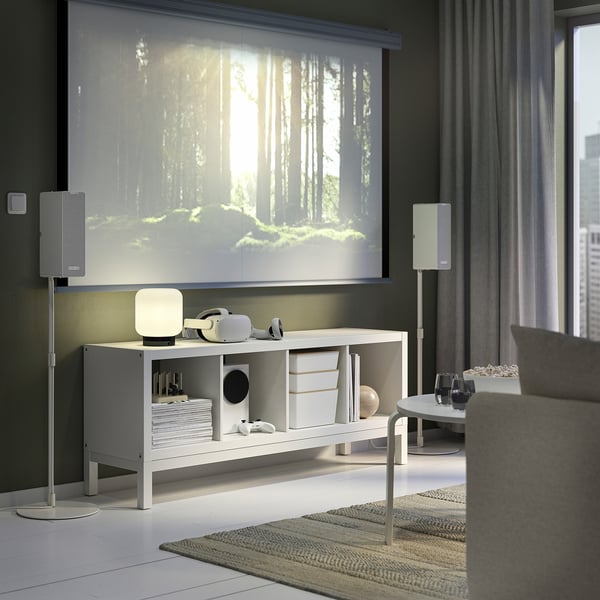Modern living room with KALLAX shelf, speakers, and forest scene on large screen, grey sofa, coffee table.