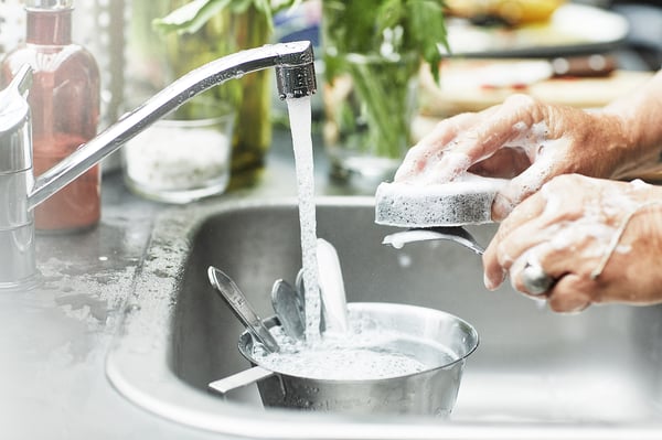 Person washing dishes in sink with running water and suds.