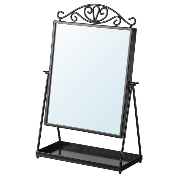A KARMSUND mirror in black with a decorative top. Its adjustable, freestanding, and a small tray at the base for storage.