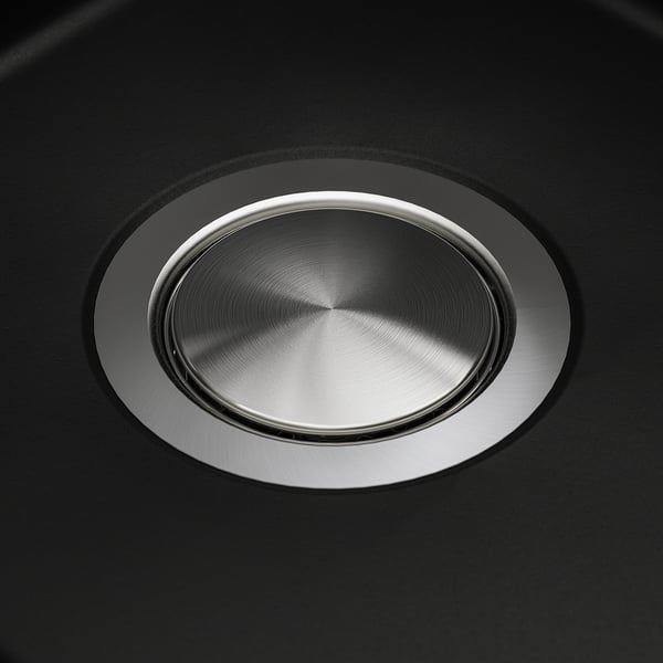 Round stainless steel sink cover on black quartz surface. Sleek, reflective design with precise craftsmanship.