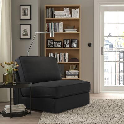 Grey KIVIK sofa-bed next to bookshelf, compact & comfy, ideal for small spaces, transforms into bed easily, sleek design with books & photos.