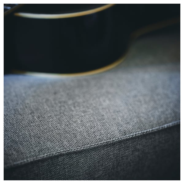 This image shows a close-up of KIVIK sofas grey, textured fabric and curved black wooden frame.