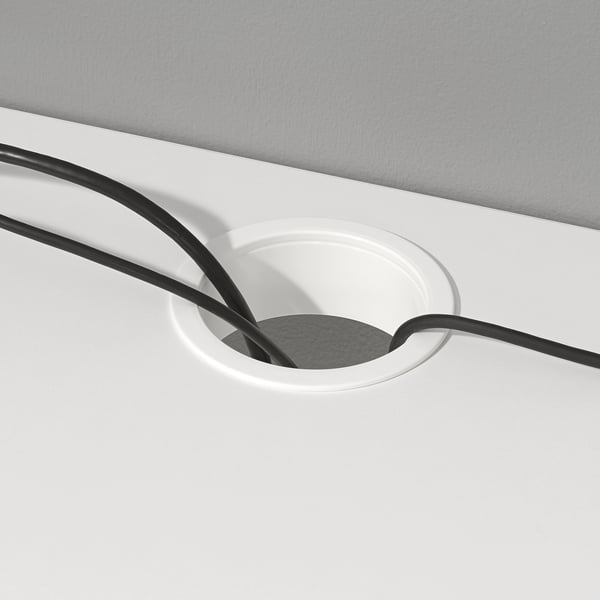 White desk with circular cable outlet, holding black cables, aiding organisation and accessibility.