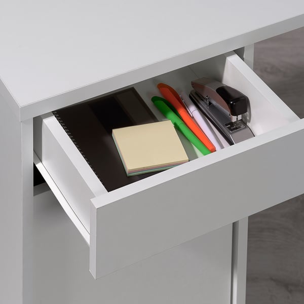 Open desk drawer holding various office supplies, including a stapler, pens, and sticky notes.