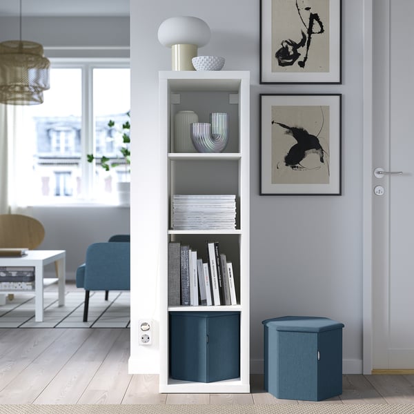 Modern living room with white KJUGE storage unit, blue pouffe, books, art, and natural light.