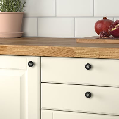 Kitchen with white drawers featuring KLINGSTORP black porcelain knobs for easy gripping. Wooden countertop with potted plant and pomegranates.