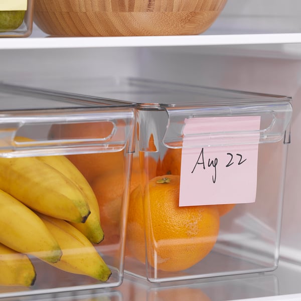 Clear fridge storage box with lid holds fruits, stacking for space efficiency, date label on handle.