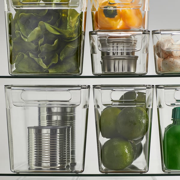 Clear plastic fridge storage boxes with lids, holding fruits, vegetables, and cans, stacking to save space.
