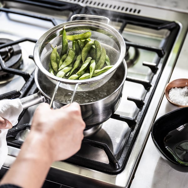Colander draining pods on stove, salt nearby.