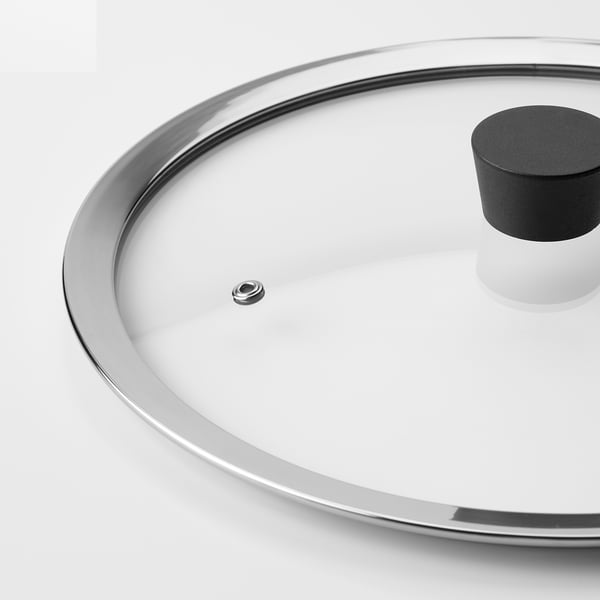 Close-up of clear, tempered glass lid with metallic rim and silicone handle, designed for cooking durability.