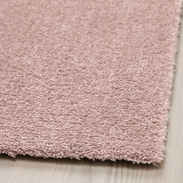 Close-up of soft, textured light pink rug on wooden floor.