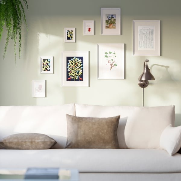 Modern living room with colourful gallery wall, green paint, white sofa, and plant.