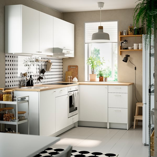 Modern l-shaped kitchen with white cabinets, oak counters, and patterned backsplash. Black-and-white flooring, with decor and greenery.