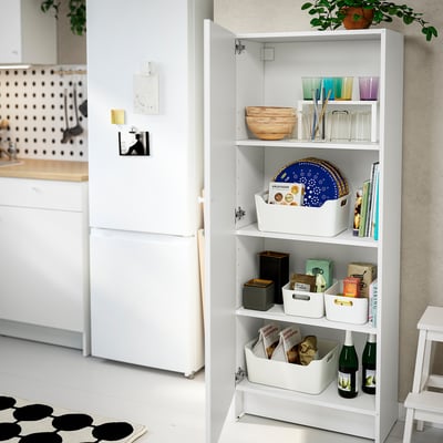 White shelf unit with adjustable shelves inside, storing glasses, bowls, books, and boxes in an organised manner.