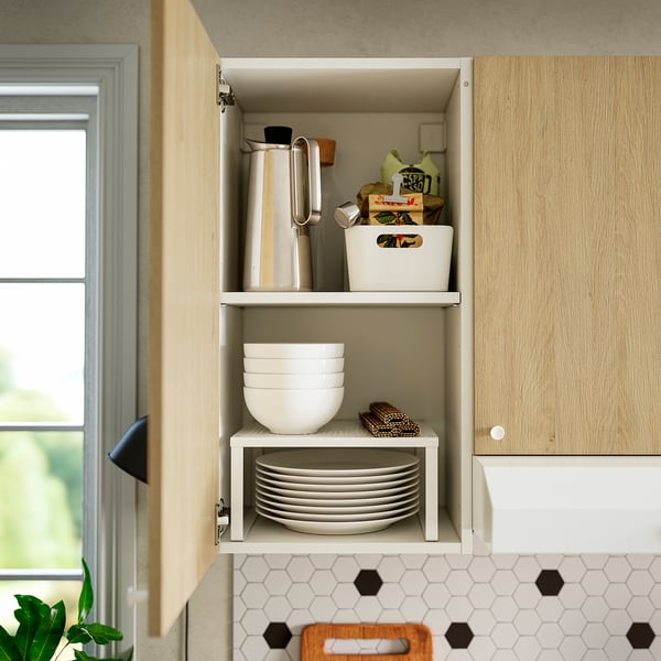 Open oak cabinet displays stacked bowls, plates, and utensils, providing easy access to kitchen items.