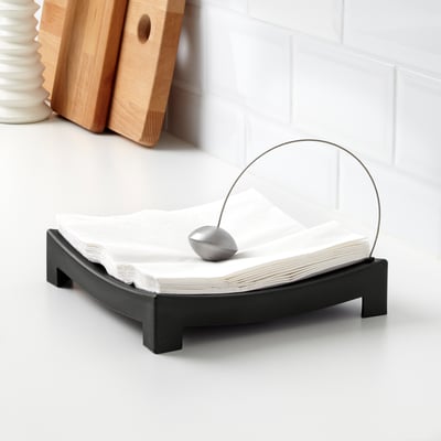 Black napkin holder with round metal rod, keeping white napkins organised on a white table.