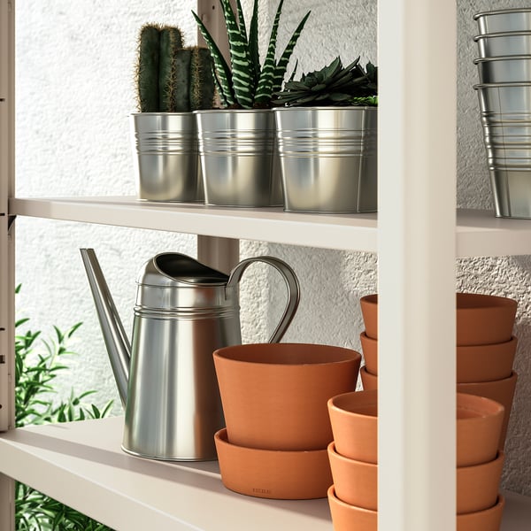 White shelving unit with terracotta pots, metal watering cans, and small potted cacti. Ideal for indoor or outdoor plant storage and organisation.