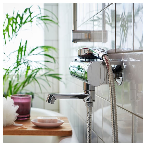 Chrome shower head with hose, tiled wall, window, plant, bath items.