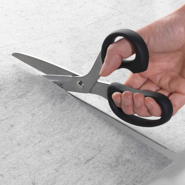 A person holds a pair of black-handled scissors, cutting a silver-colored sheet on a countertop.