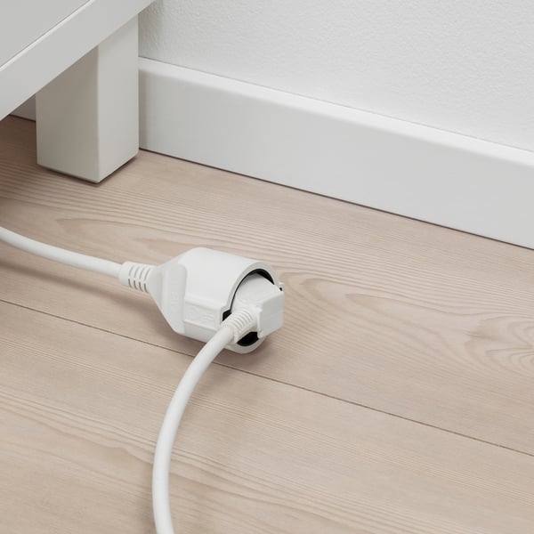 White extension cord on wooden floor, plugged in, providing power access.