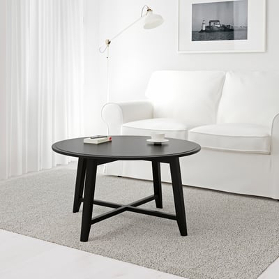 Modern living room with a round black coffee table holding a mug and a book. Beside a white armchair under a wall lamp.