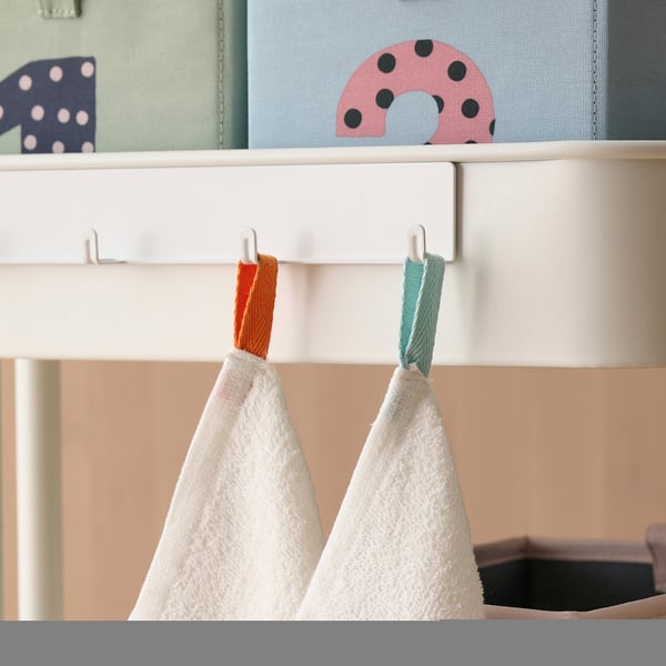 Two white towels hang from colourful hooks on a white shelf. The hooks add vibrant colour to the neutral shelf.