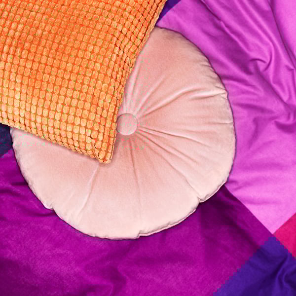 Bright decorative cushions, including a round light pink and an orange patterned pillow, set against a purple background.