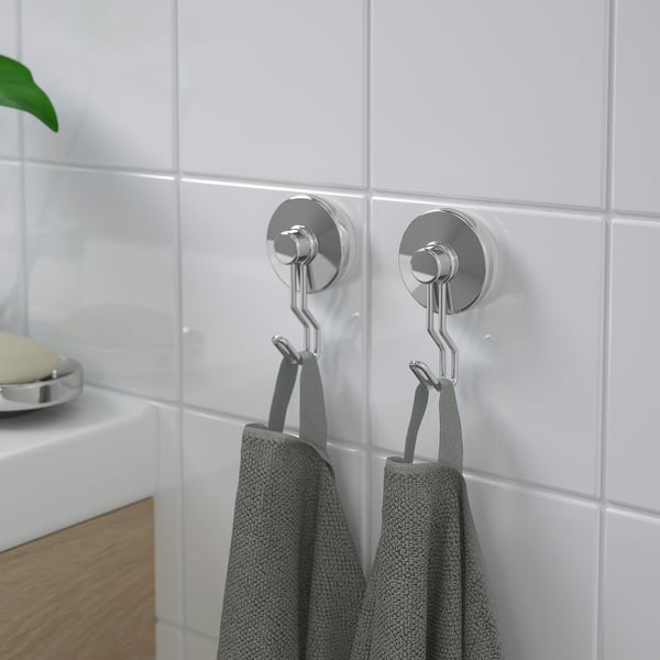 Two silver suction cup hooks hang grey towels on a white tiled wall, providing organised bathroom storage without needing drilling.