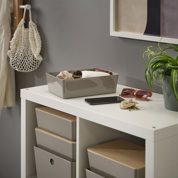 White desk with a storage box, sunglasses, keys, and a phone on top. A plant is beside them.