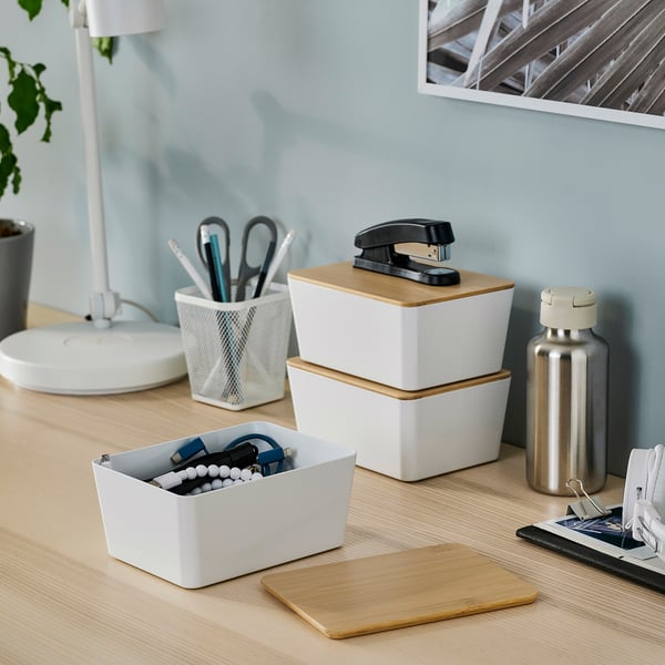 Organised desk with KUGGIS boxes in white; small, white box for cables, larger boxes stacked with black stapler top.