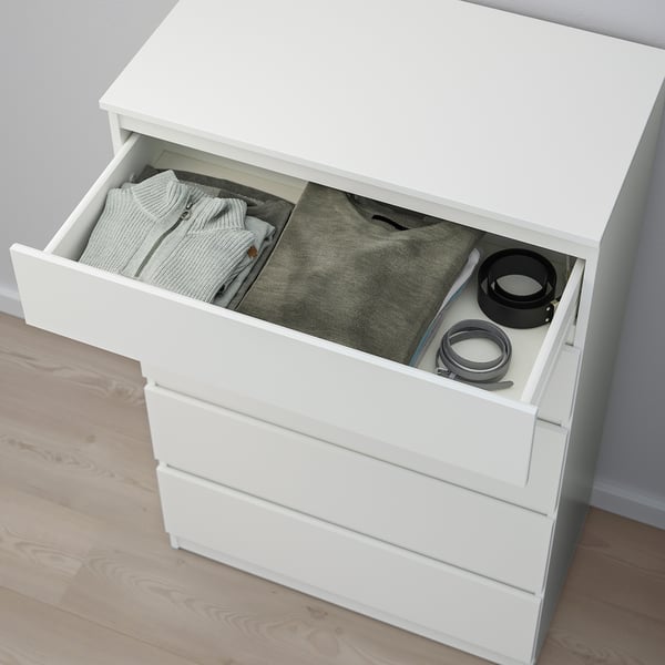 White chest of drawers with an open drawer revealing folded clothes and small items. It includes an anchoring kit for safety.