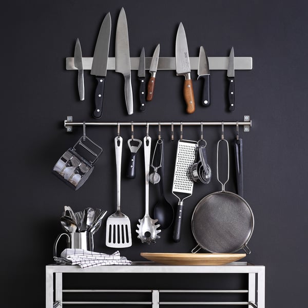 Wall-mounted kitchen storage with knives, utensils, and holder on dark background.