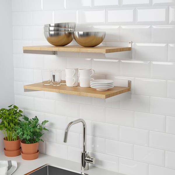 Wooden wall shelves hold metal bowls and white mugs, saving countertop space in a kitchen with white subway tiles and stainless steel tap.