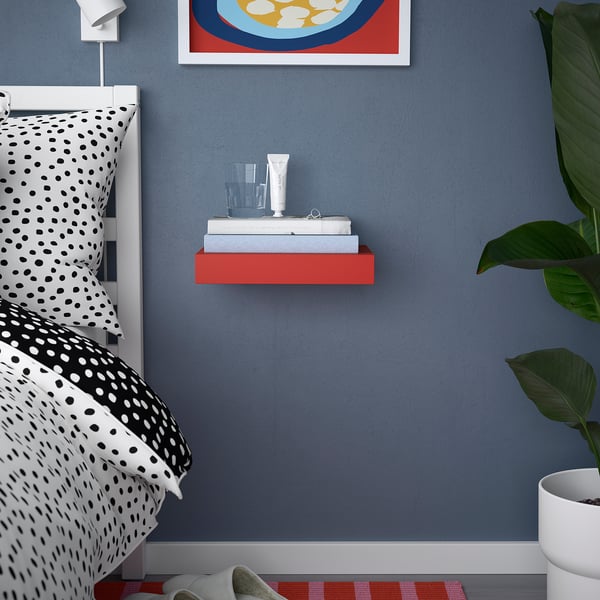 Blue bedroom with red shelf, spotted bedding, plant, and artwork.