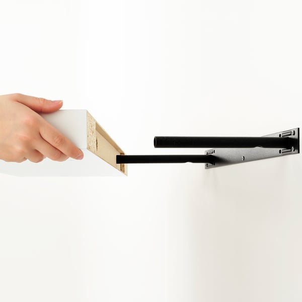 A hand places a square, wooden-finished LACK shelf onto a wall-mounted, bLACK metal bracket, revealing the shelfs hidden suspension hardware.
