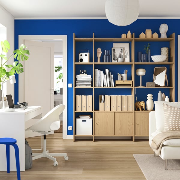 Modern home office with blue accent wall, light wood bookshelf, white desk, and chair.