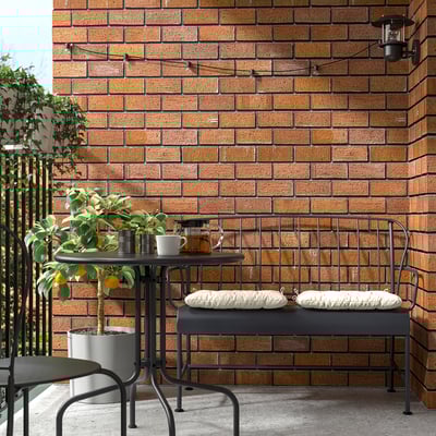 Small outdoor table set. Black metal design. Against brick wall. With two cushioned benches. Next to potted lemon tree.