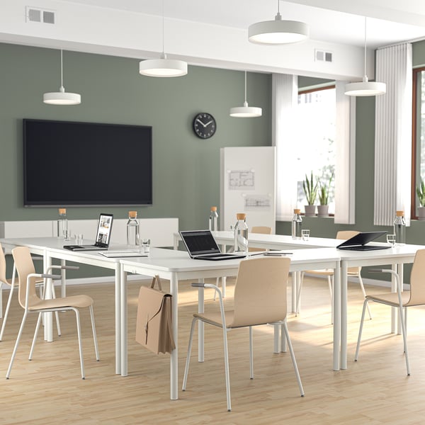 Modern conference room with white tables, cream chairs, green walls, two tvs. Neat arrangement, wooden floor.