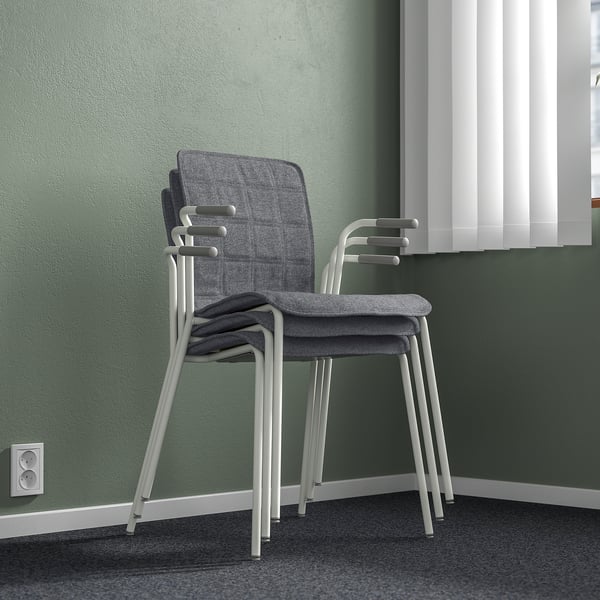 Stacked modern office chairs, light grey with white legs, stacked three high against green wall.