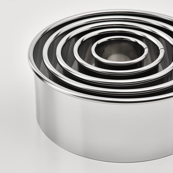 Stack of shiny stainless steel cookie cutters in varying sizes, reflecting light.