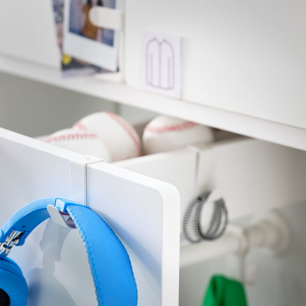 Blue headphones hang on a white hook mounted on a shelf unit.