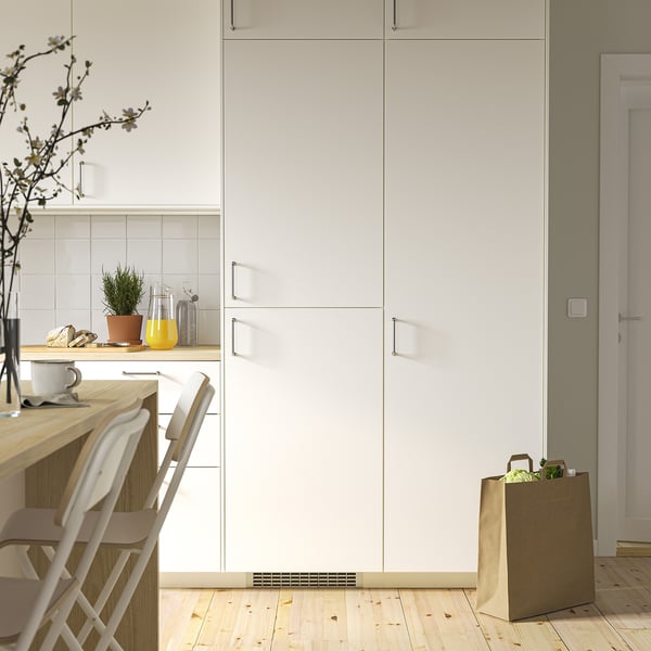 Modern white fridge embedded in kitchen cabinets, smaller than adjacent chairs and countertop items.