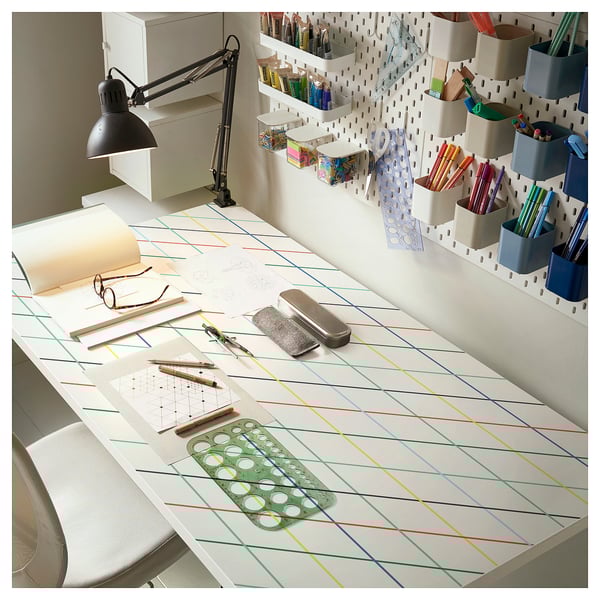 Modern white desk with colourful grid pattern. Includes lamp, various art supplies, and pegboard with organisers. Perfect for crafting or study.